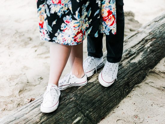 Couple Standing on Log at the Beach, Wearing White Sneakers.