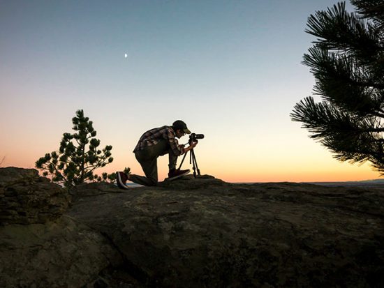 Man at sunset taking a photo with a camera on a tripod