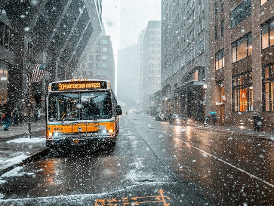 Boston street in winter, snow falling and a bus in the street.