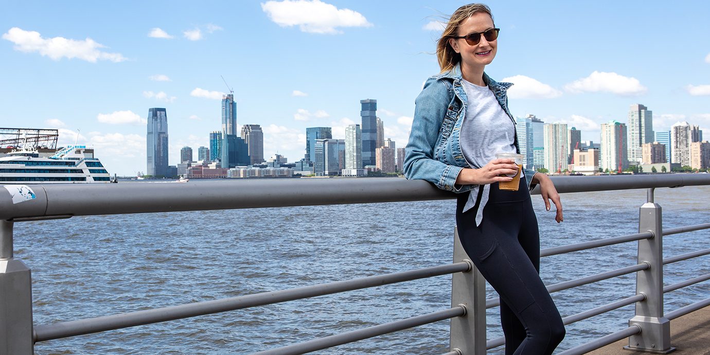 Megan Standing on a Pier in Manhattan with Coffee in Hand, Wearing Fabletics Leggings.