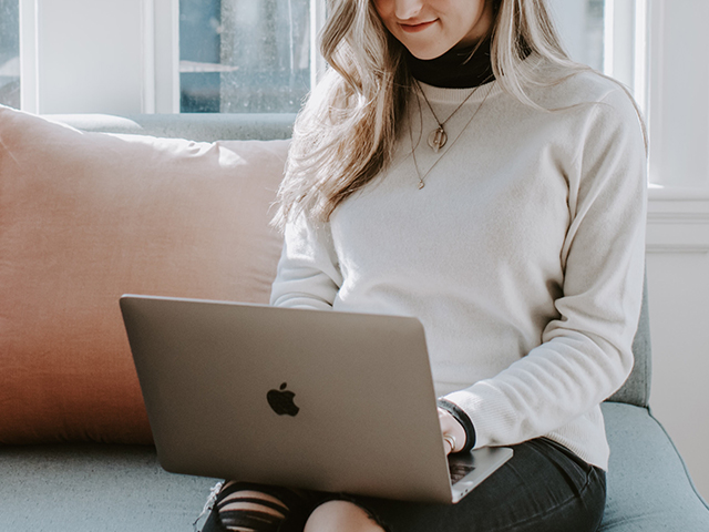 Woman seated on a couch using a laptop.