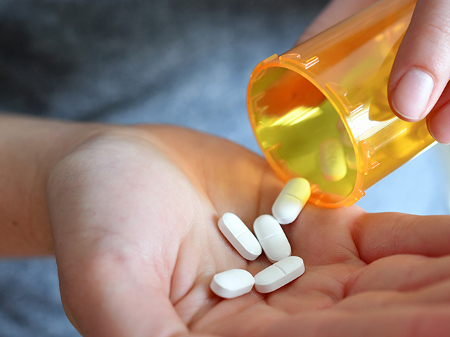 Man shaking pills into his hand from a bottle.